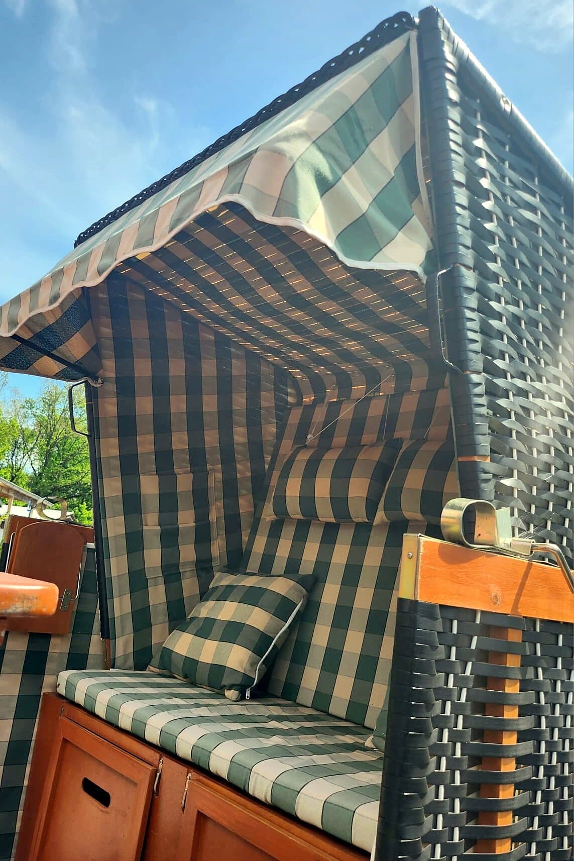 Karierter Strandkorb auf der Terrasse: grün-weiß kariert mit Kissen, darüber blauer Himmel